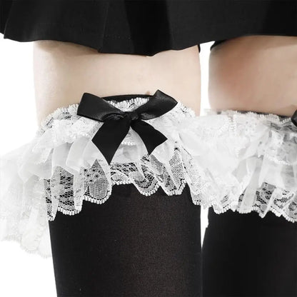 White lace garter stockings with ruffled tulle and black satin bows, worn on legs with black tights.