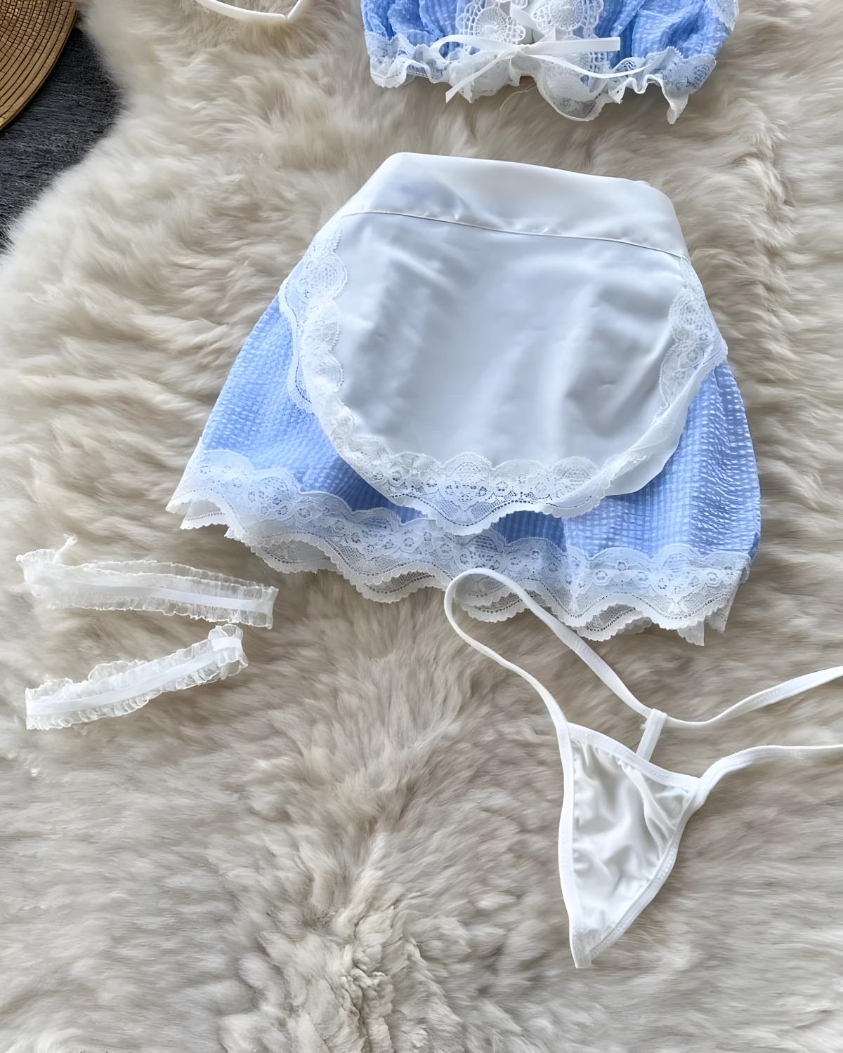 A blue and white lingerie set laid flat on a fluffy cream faux-fur surface, including a lace-trimmed white apron-style top, matching blue mesh bottoms, white lace garter straps, and a white satin thong.