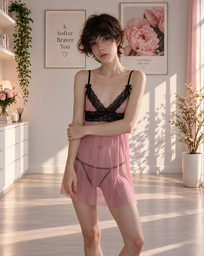 A woman stands in a sunlit bedroom wearing a sheer pink lingerie set with black lace trim and black undergarments. Framed wall art, shelves, and potted plants are visible in the room.