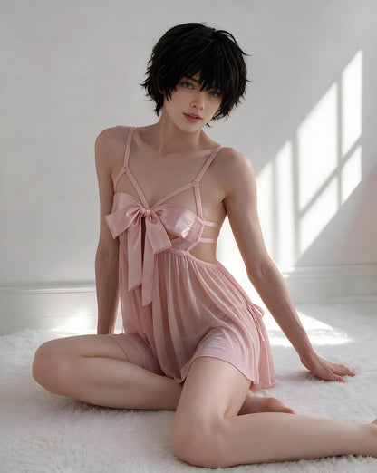 A model with short black hair sits on a white shag rug wearing a light pink satin slip dress with a large bow at the chest and sheer side cutouts, set against a bright white wall with window light shadows.