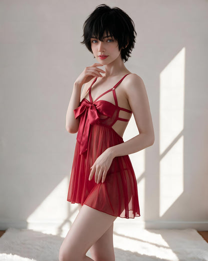 A woman modeling a red sheer babydoll lingerie dress with strappy details and a large bow at the bust, posed in a brightly lit room with window shadows.
