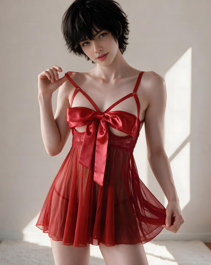 A woman modeling a red sheer babydoll lingerie dress with a satin bow at the bust, photographed in a softly lit indoor setting with warm sunlight and shadows.
