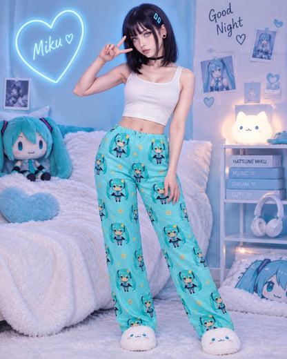 A woman stands in a bedroom setting wearing light blue pajama pants with a repeating Hatsune Miku character print, paired with a white crop top and white slippers. The room is decorated with Hatsune Miku-themed items, including a plush doll, a glowing heart-shaped sign, and shelves with books and headphones.