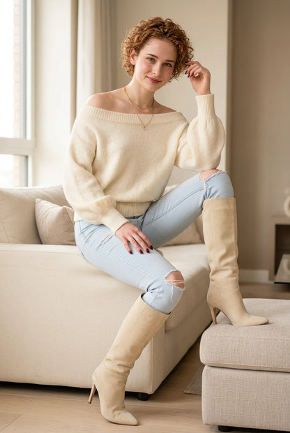 Oversized ivory off shoulder sweater with light-wash jeans and cream boots, seated lifestyle view