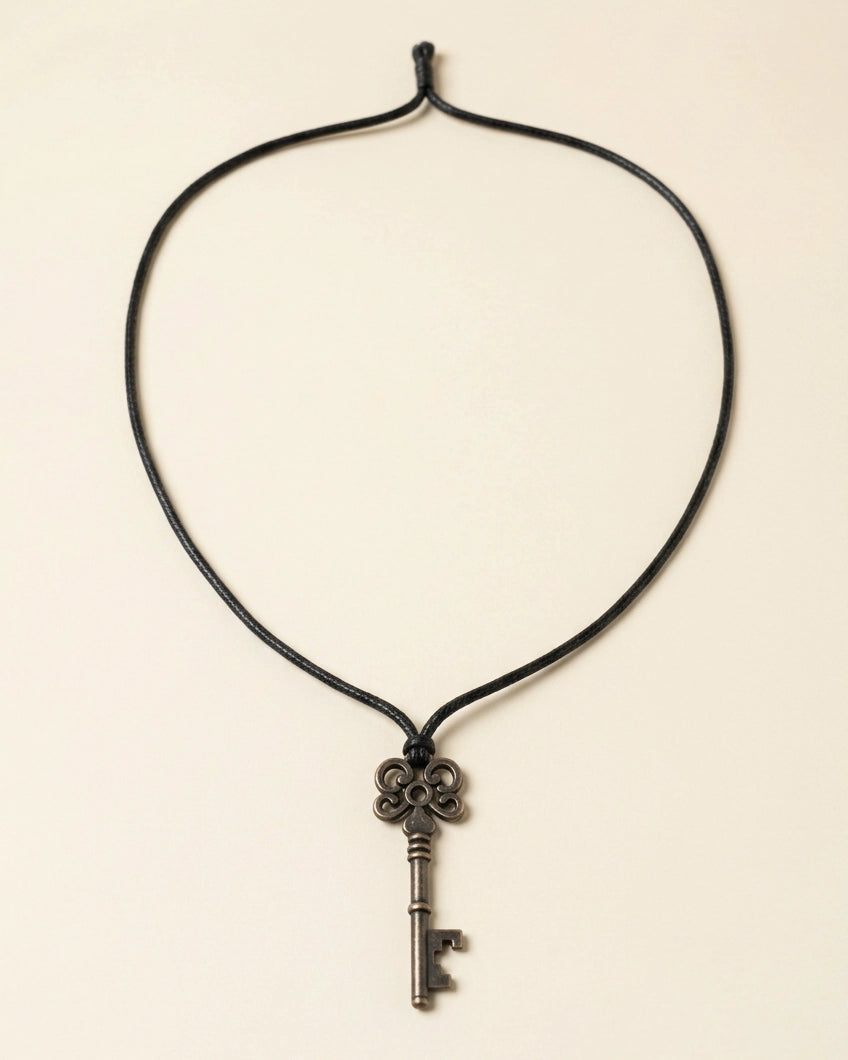A black cord necklace featuring an antique-style metal key pendant, displayed against a solid light beige background.
